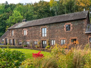 A stone house with multiple windows and greenery in front at Bank Barn Wreay in Watermillock