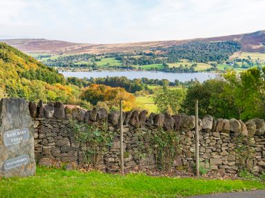 A stone wall with a sign reading Bank Barn Wreay private property and a view of a lake and hills in the background at Bank Barn Wreay in Watermillock