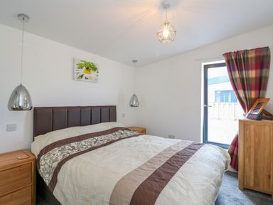 A bedroom with a bed between two wooden bedside tables and a cabinet near a window at 6 Strathtay Lodges in Aberfeldy