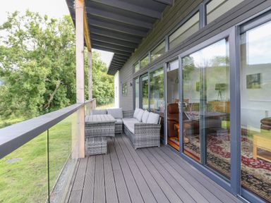 A balcony with a wicker sofa set and glass railing overlooking trees at 6 Strathtay Lodges in Aberfeldy