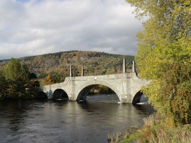 A stone arch bridge over a river with trees and forested hills in the background at 6 Strathtay Lodges in Aberfeldy