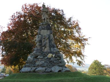 A stone statue monument with a carved figure on top and trees in the background at 6 Strathtay Lodges Aberfeldy