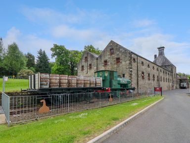 An outdoor scene with a vintage train carrying barrels next to a stone building at 6 Strathtay Lodges in Aberfeldy