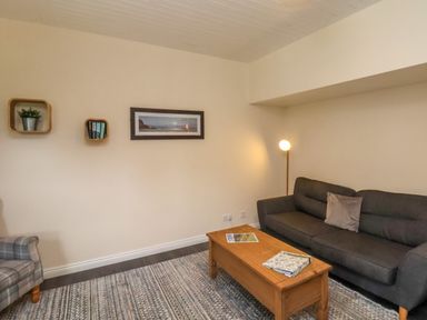 A living room with a dark gray sofa a wooden coffee table a floor lamp and wall shelves at Cowslip in Saltburn-By-The-Sea