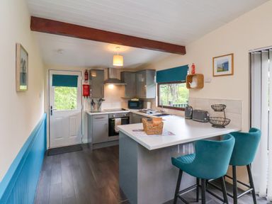 A kitchen with gray cabinets a white countertop two teal chairs and a door with a blue blind at Cowslip in Saltburn-By-The-Sea