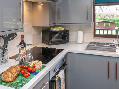 A kitchen with gray cabinets a black microwave a stovetop a bread loaf tomatoes a bottle of wine and two wine glasses at Cowslip in Saltburn-By-The-Sea