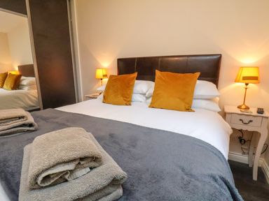 A bedroom with a double bed two orange pillows bedside tables with lamps and folded towels at Cowslip in Saltburn-By-The-Sea