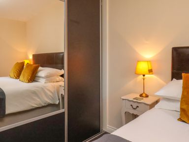 A bedroom with a bed with mustard pillows a bedside table with a lamp and a mirrored wardrobe at Cowslip in Saltburn-By-The-Sea