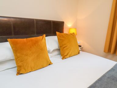 A bed with two mustard color pillows a bedside table with a lamp and a curtain at Cowslip in Saltburn-By-The-Sea