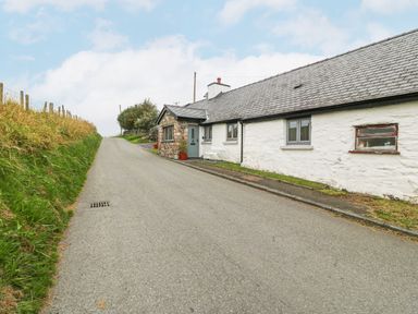 A narrow paved road with grass on the side and a white stone house with grey windows at Penrallt in Rhydlydan