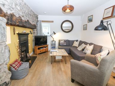 A living room with a stone fireplace a gray couch a wooden coffee table and a TV at Penrallt in Rhydlydan