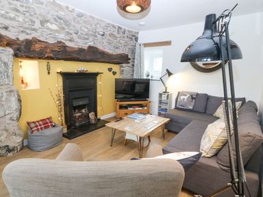A living room with a stone wall fireplace television wooden coffee table and grey sofa at Penrallt in Rhydlydan