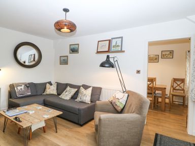 A living room with a gray sofa a beige armchair a wooden coffee table and a dining area visible through a doorway at Penrallt in Rhidlydan
