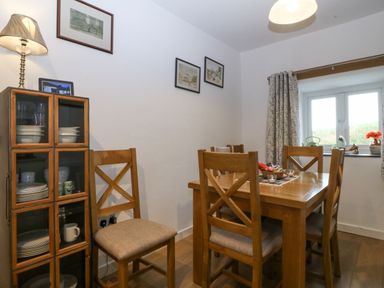 A dining room with wooden table and chairs a glass cabinet with dishes and a window with curtains at Penrallt in Rhydlydan