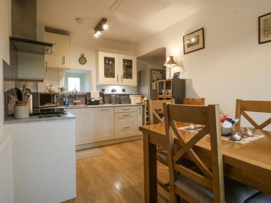A kitchen with white cabinets wooden dining table and chairs and kitchen appliances at Penrallt in Rhydlydan