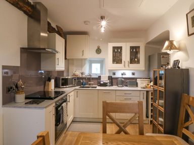 A kitchen with white cabinets a microwave and toaster and a dining table with wooden chairs at Penrallt in Rhydlydan