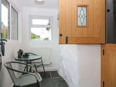 A small dining area with a round glass table and two chairs next to a wooden cupboard at Penrallt in Rhydlydan