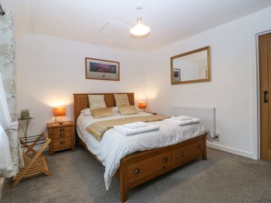 A bedroom with a double bed bedside tables with lamps a wall mirror and a wooden door at Penrallt in Rhydlydan