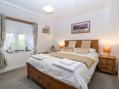 A bedroom with a double bed two bedside tables with lamps a window with curtains and framed pictures on the walls at Penrallt in Rhydlydan
