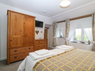 A bedroom with a wooden wardrobe and chest of drawers a bed with folded towels and windows with curtains at Penrallt in Rhydlydan