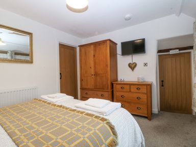 A bedroom with wooden wardrobe and dresser a wall mounted TV and a bed with folded towels at Penrallt in Rhydlydan