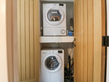 A laundry closet with a stacked washer and dryer and cleaning supplies at Penrallt in Rhydlydan
