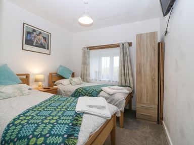 A bedroom with two single beds a wooden wardrobe a window with curtains and a bedside table with a lamp at Penrallt in Rhydlydan