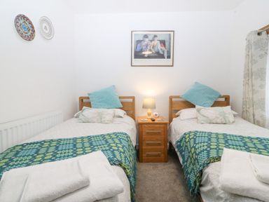A bedroom with two single beds a wooden nightstand with a lamp between them and decorative plates on the wall at Penrallt in Rhydlydan