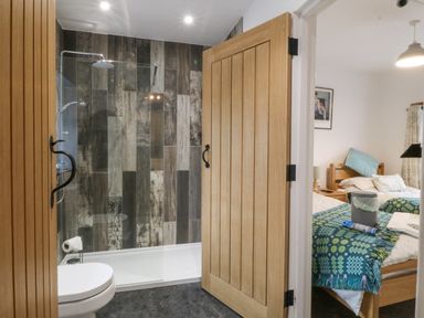 A bathroom with a shower and toilet next to a bedroom with two beds at Penrallt in Rhydlydan
