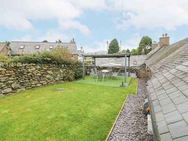 A backyard with green grass stone wall a patio set with chairs under a pergola at Penrallt in Rhydlydan