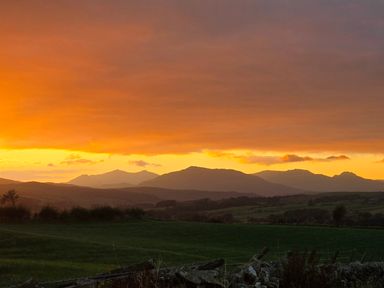 A sunset over mountains with green fields and a stone fence at Penrallt in Rhydlydan