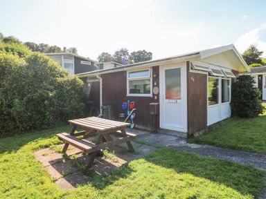 A small brown wooden house with white trim and a picnic table outside on a grassy area at Milkwood in Elmrise Park near Llansteffan