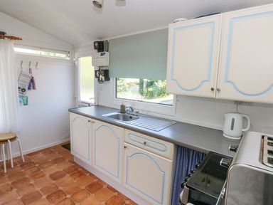 A kitchen with white cabinets a countertop sink kettle and toaster at Milkwood in Elmrise Park near Llansteffan