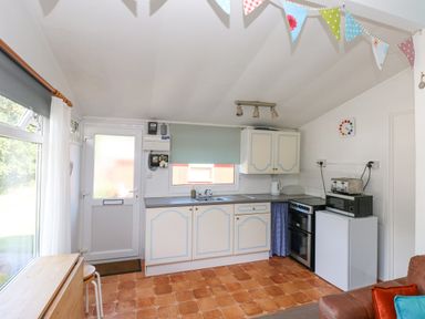 A kitchen with white and blue cabinets a stove a refrigerator a toaster and a kettle at Milkwood in Elmrise Park near Llansteffan