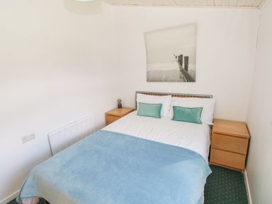 A bedroom with a double bed blue blanket and two wooden bedside tables at Milkwood in Elmrise Park near Llansteffan