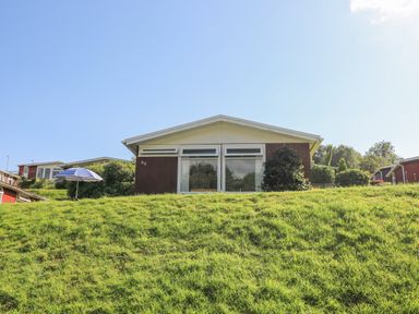 A small house with large windows on a grassy slope at Milkwood in Elmrise Park near Llansteffan