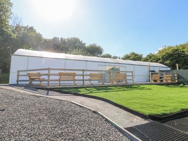 An outdoor seating area with wooden benches on a raised wooden deck next to a large white tent structure at Milkwood in Elmrise Park near Llansteffan
