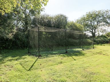 A cricket practice net on a grassy field surrounded by trees at Milkwood in Elmrise Park near Llansteffan