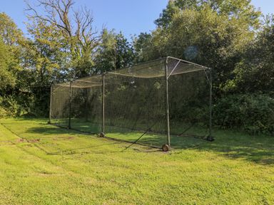 An outdoor cricket practice net on a grassy field with trees in the background at Milkwood in Elmrise Park near Llansteffan