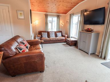 A living room with brown leather sofas a wall mounted television and a cabinet at Brightwater Lodge White Cross Bay near Windermere