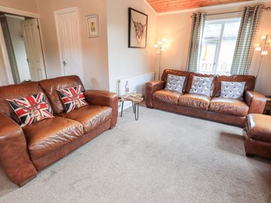A living room with two brown leather sofas a small wooden side table and a window with checkered curtains at Brightwater Lodge White Cross Bay near Windermere