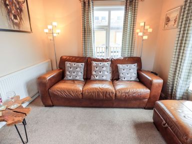 A living room with a brown leather sofa and three sheep pattern cushions at Brightwater Lodge White Cross Bay near Windermere
