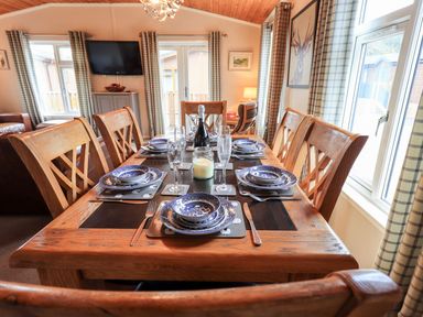 A dining room with a wooden table set with plates glasses and cutlery and plaid curtains at Brightwater Lodge White Cross Bay near Windermere