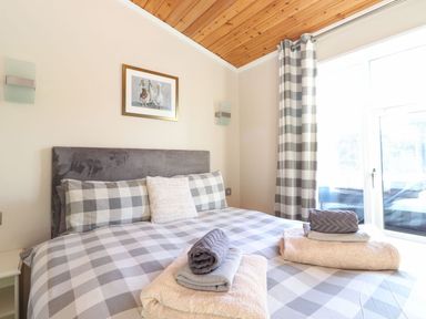 A bedroom with a double bed covered in checkered bedding two sets of folded towels on the bed framed picture of ducks on the wall and checkered curtains at Brightwater Lodge White Cross Bay near Windermere
