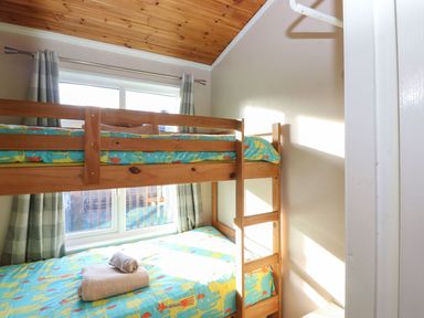 A small bedroom with wooden bunk beds covered in colorful animal print bedding near a window with curtains at Brightwater Lodge White Cross Bay near Windermere