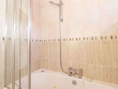 A bathroom with a bathtub shower and tiled walls at Brightwater Lodge in White Cross Bay near Windermere