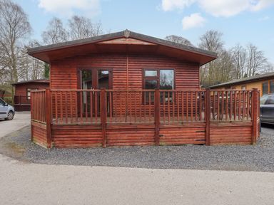 A wooden cabin with a fenced deck and gravel driveway at Brightwater Lodge in White Cross Bay near Windermere