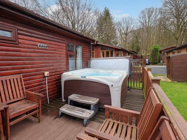 An outdoor wooden deck with a hot tub and wooden chairs at Brightwater Lodge in White Cross Bay near Windermere