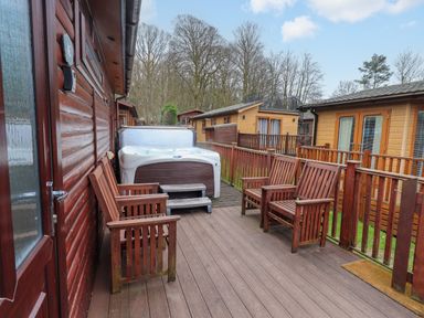 A wooden deck with four wooden chairs and a hot tub near wooden lodges at Brightwater Lodge White Cross Bay near Windermere
