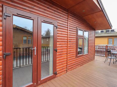 A wooden deck with glass double doors and a window on a log cabin exterior at Brightwater Lodge White Cross Bay near Windermere